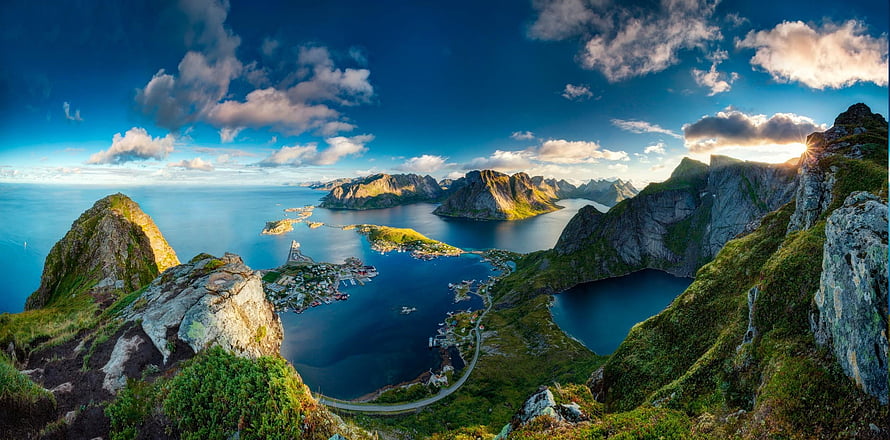 Stunning panoramic view of Reine village in the Lofoten Islands, Norway, featuring dramatic mountains, a serene fjord, and a vibrant sunset sky HD wallpaper