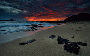 Dramatic Crimson Sunset Over Rocky Shoreline with Dark Volcanic Stones on Sand HD wallpaper