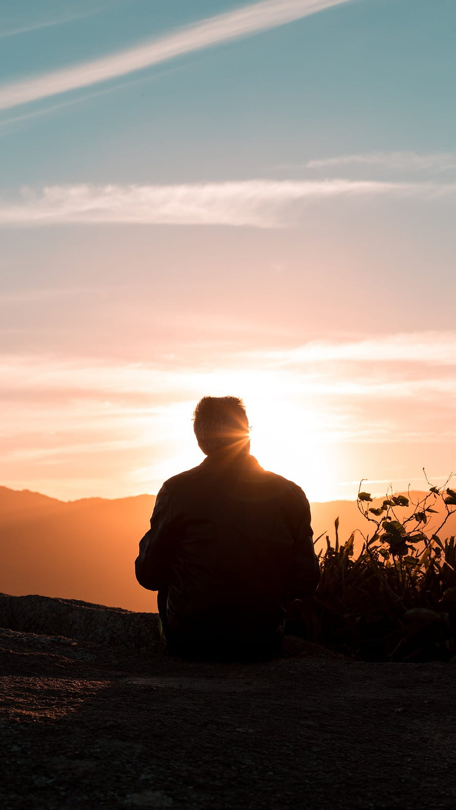 Silhouette of a person sitting on a hilltop watching a golden sunset over distant mountains HD phone wallpaper