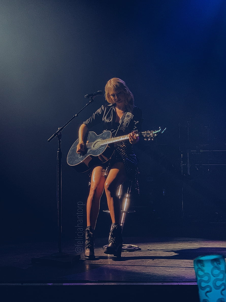 Taylor Swift performing acoustic set on stage with guitar and microphone under dramatic blue lighting HD phone wallpaper