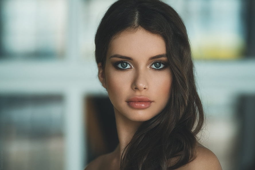 Close-up portrait of a woman with dark wavy hair and striking blue eyes against a soft blurred background, Unknown Model, gorgeous, model, beautiful, woman HD wallpaper