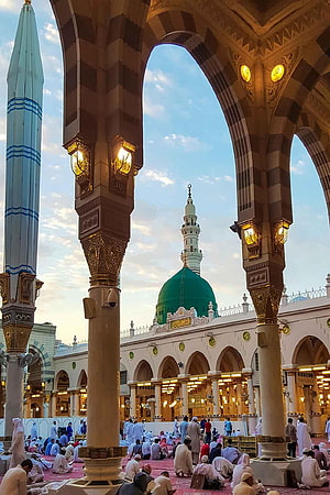 The Green Dome of Al-Masjid an-Nabawi in Medina framed by striped arches and worshippers HD phone wallpaper