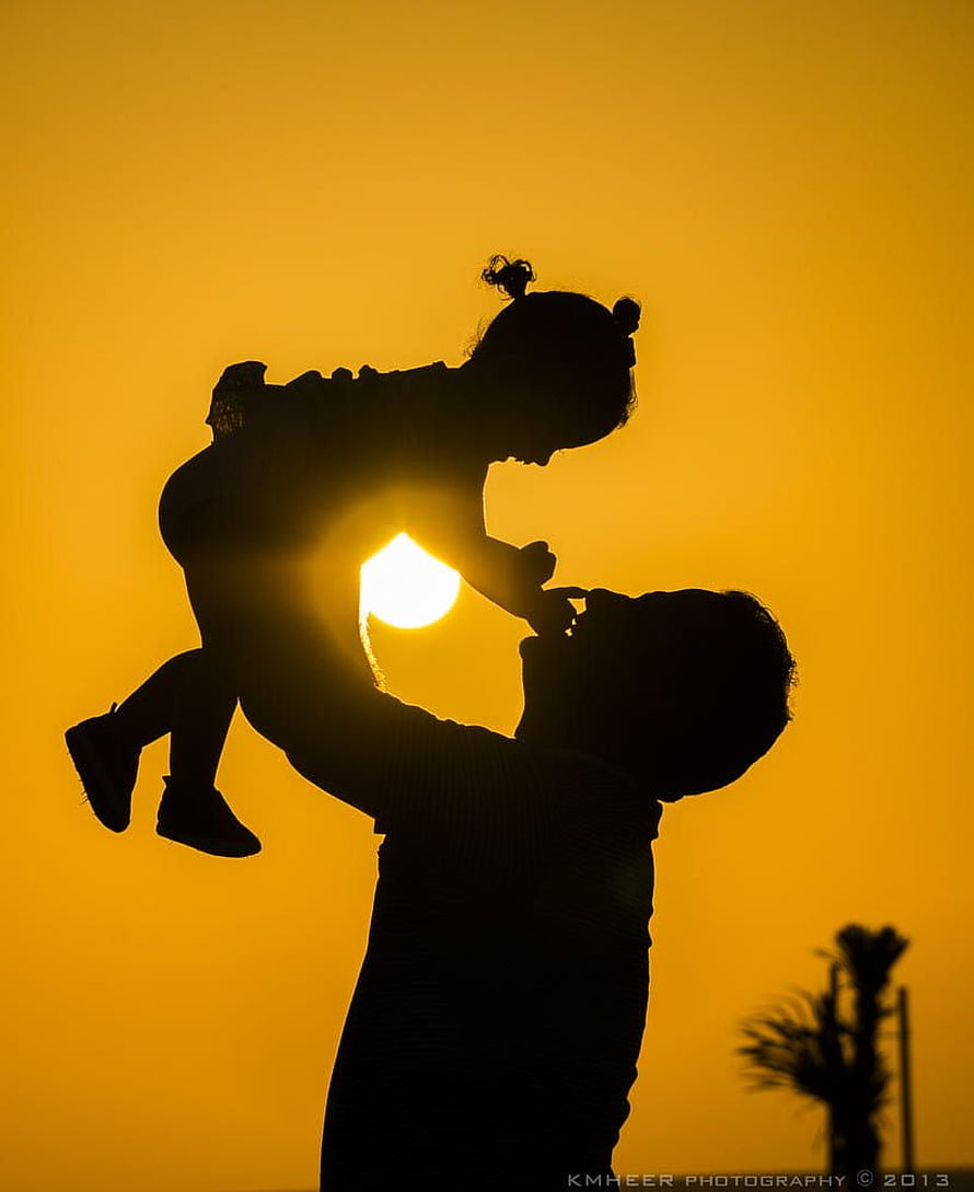Silhouette of a father lifting his young daughter against a golden sunset sky HD phone wallpaper
