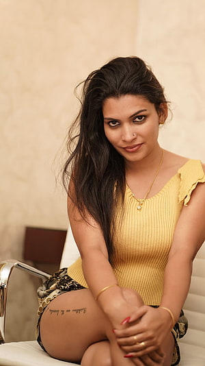 Reshmi Nair in a yellow ribbed top and patterned shorts, seated portrait with gold jewelry HD phone wallpaper