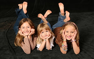 Three young girls lying on their stomachs with feet up in a studio portrait HD wallpaper