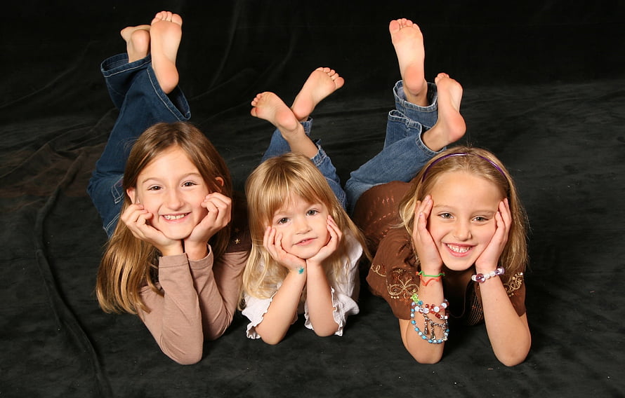 Three young girls lying on their stomachs with feet up in a studio portrait HD wallpaper