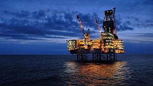 Illuminated Offshore Oil Rig at Night with Warm Lights Reflecting on the Ocean HD wallpaper
