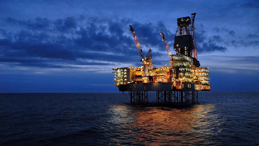 Illuminated Offshore Oil Rig at Night with Warm Lights Reflecting on the Ocean HD wallpaper