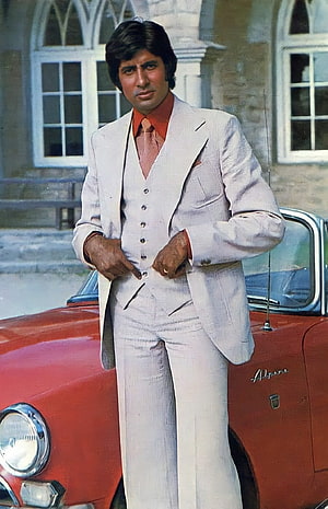 Amitabh Bachchan in a white three-piece suit standing beside a vintage red car HD phone wallpaper