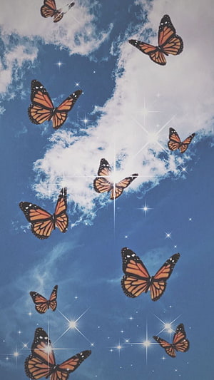 Monarch butterflies soaring through a blue sky with soft clouds and sparkling light effects HD phone wallpaper