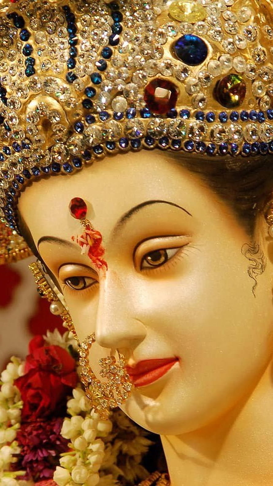 Close-up of a beautifully adorned Hindu goddess statue with jeweled crown and floral garlands HD phone wallpaper