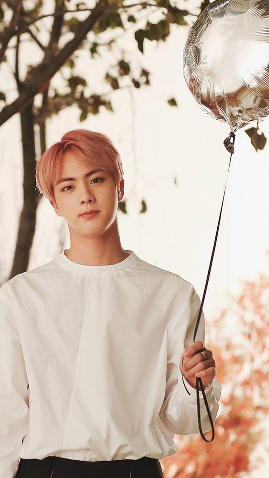 Jin from BTS holding a silver balloon in a white shirt with autumn foliage background HD phone wallpaper