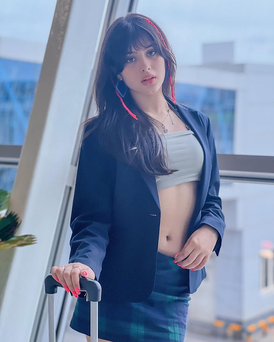 Riva Arora in navy blazer and plaid skirt holding a suitcase handle HD phone wallpaper