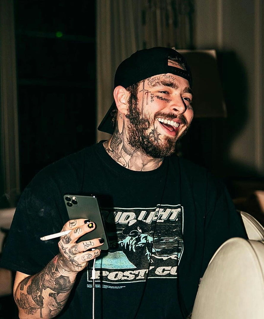 Post Malone smiling while holding a smartphone and wearing a black graphic t-shirt HD phone wallpaper