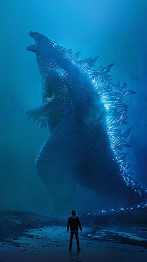 Godzilla standing on a dark beach with glowing blue dorsal fins facing a lone figure HD phone wallpaper