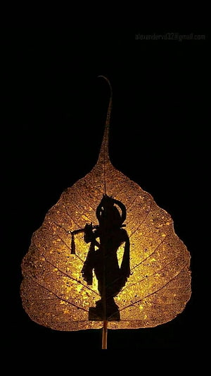 Silhouette of Hindu deity Krishna playing flute on backlit golden peepal leaf art HD phone wallpaper
