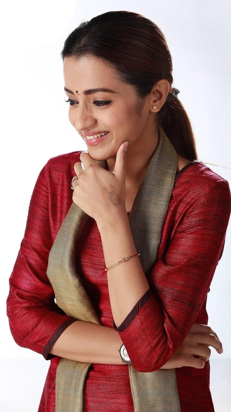Trisha Krishnan in a red kurta with a gold scarf, smiling softly with a thoughtful pose HD phone wallpaper