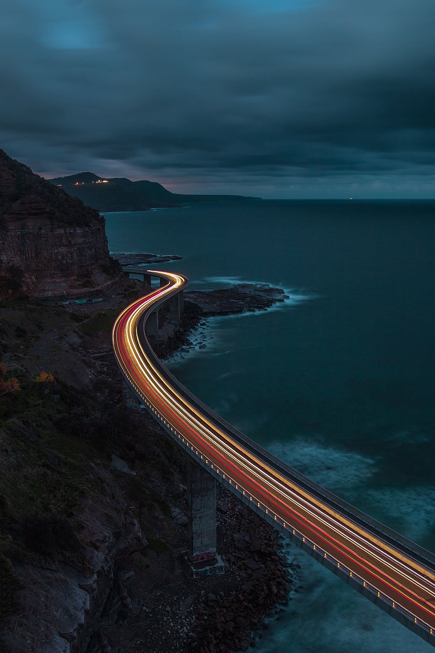 Coastal Highway Bridge at Dusk with Long Exposure Light Trails Over the Ocean HD phone wallpaper