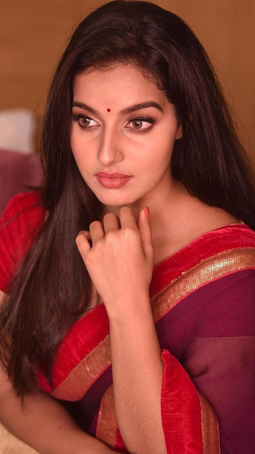 Malavika Menon in a red and purple saree with gold border, hand resting near chin, warm indoor portrait HD phone wallpaper