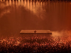 Kanye West Seated on Floating Stage Above Massive Concert Crowd in Dramatic Orange Light HD wallpaper