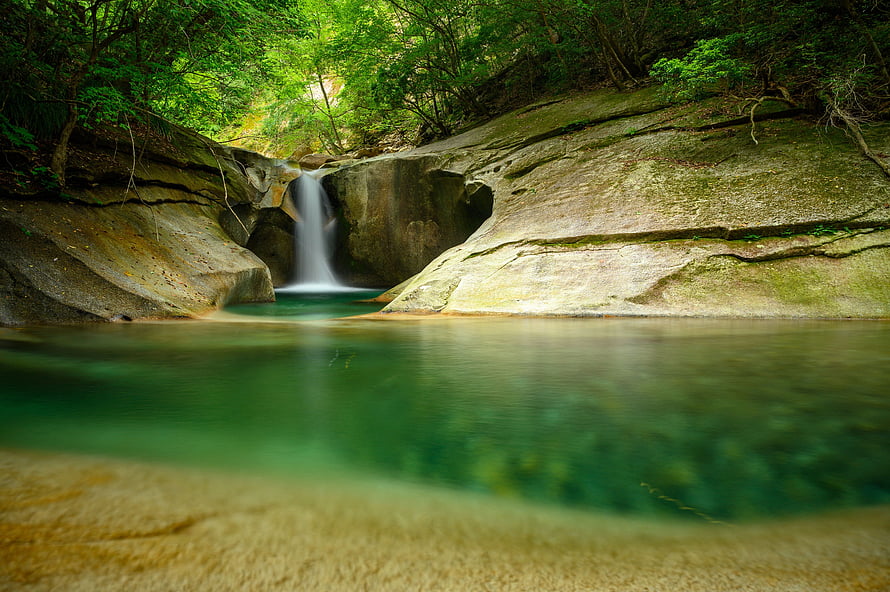 Serene Forest Waterfall Cascading Into a Turquoise Pool Surrounded by Lush Greenery and Smooth Rocks HD wallpaper