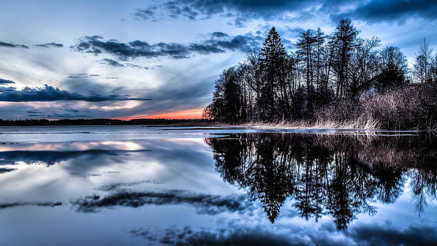 Serene Frozen Lake at Dusk with Pine Tree Reflections and Dramatic Clouds HD wallpaper