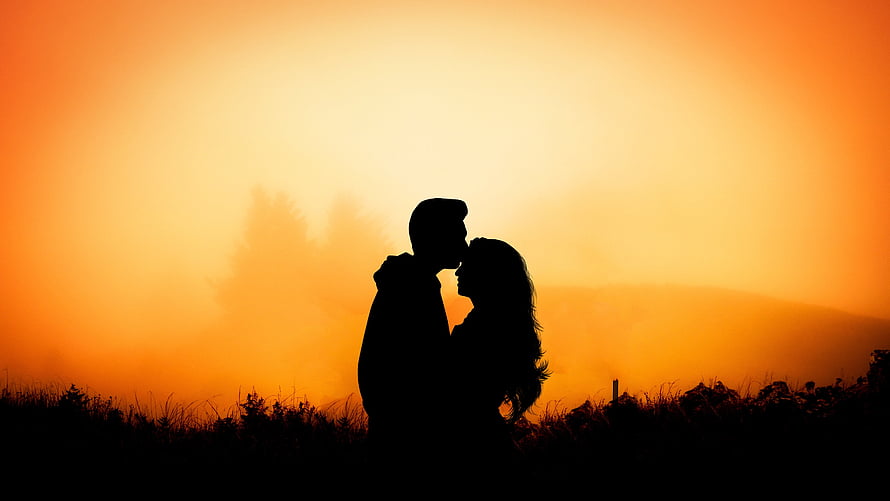 Romantic Couple Silhouette Sharing a Kiss Against a Golden Sunset Sky HD wallpaper