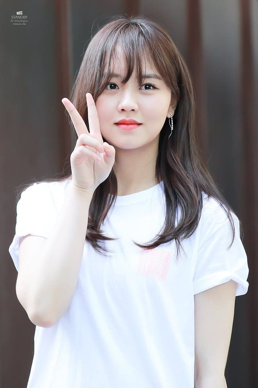 Kim So Hyun in a white t-shirt making a peace sign with long brown hair and bangs HD phone wallpaper