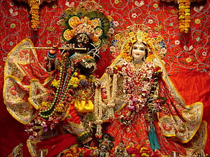 Radha Krishna idols adorned with flowers and jewelry on a red embroidered backdrop HD wallpaper