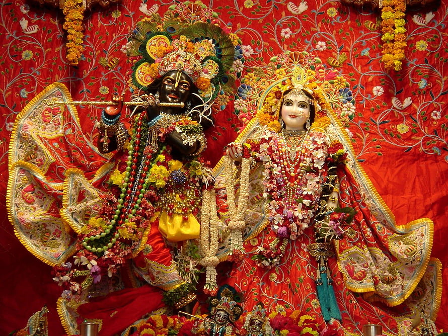 Radha Krishna idols adorned with flowers and jewelry on a red embroidered backdrop HD wallpaper