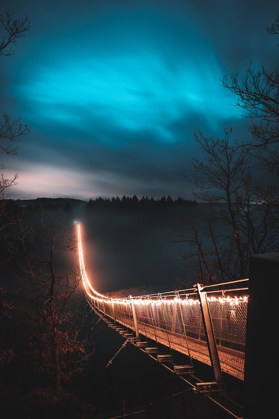 Illuminated suspension bridge at night with glowing lights and blue aurora sky HD phone wallpaper