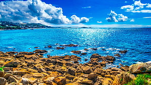 Sunny Coastal View With Rocky Shoreline And Bright Blue Sea Under Cloudy Sky HD wallpaper