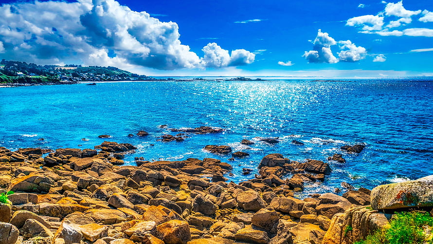 Sunny Coastal View With Rocky Shoreline And Bright Blue Sea Under Cloudy Sky HD wallpaper