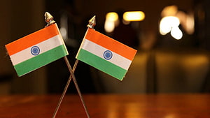 Two Small Indian National Flags Crossed on a Wooden Table with Warm Bokeh Background HD wallpaper