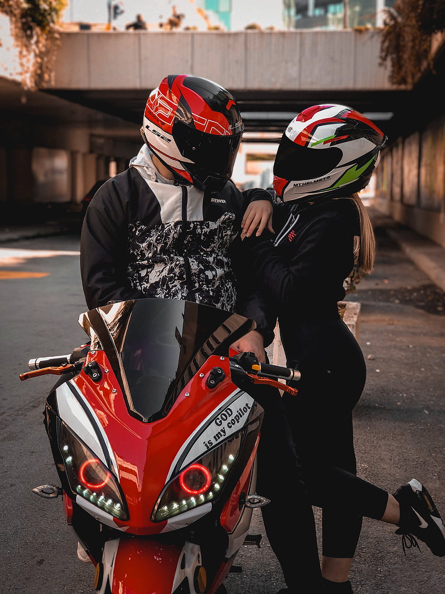 Couple in Full Face Helmets Posing with Red Sport Motorcycle Under Urban Overpass HD phone wallpaper
