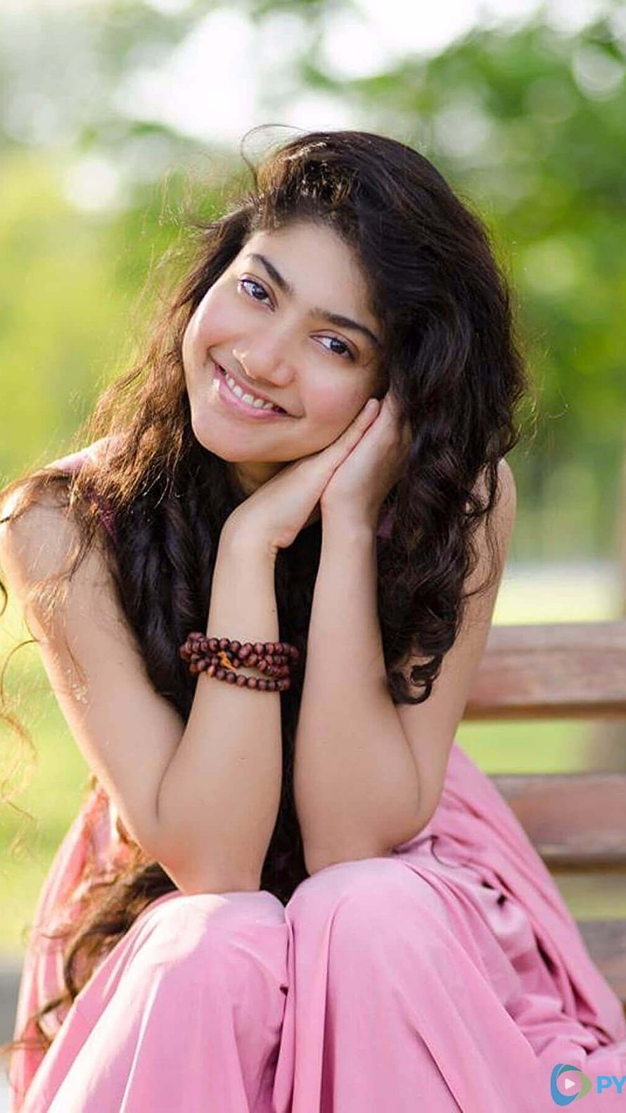 Sai Pallavi in a pink dress smiling outdoors with long wavy hair and wooden beads bracelet HD phone wallpaper