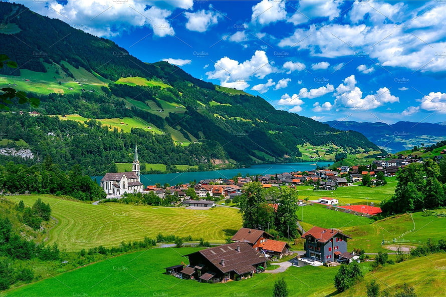 Scenic View of a Swiss Village with Church and Lake Surrounded by Green Mountains HD wallpaper