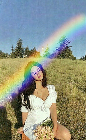 Lana Del Rey in a white dress sitting in a grassy field with a rainbow and wildflowers HD phone wallpaper