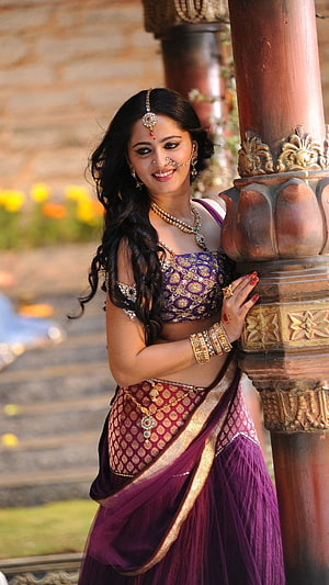 Anushka Shetty in Traditional Purple Saree with Gold Jewelry and Temple Architecture HD phone wallpaper