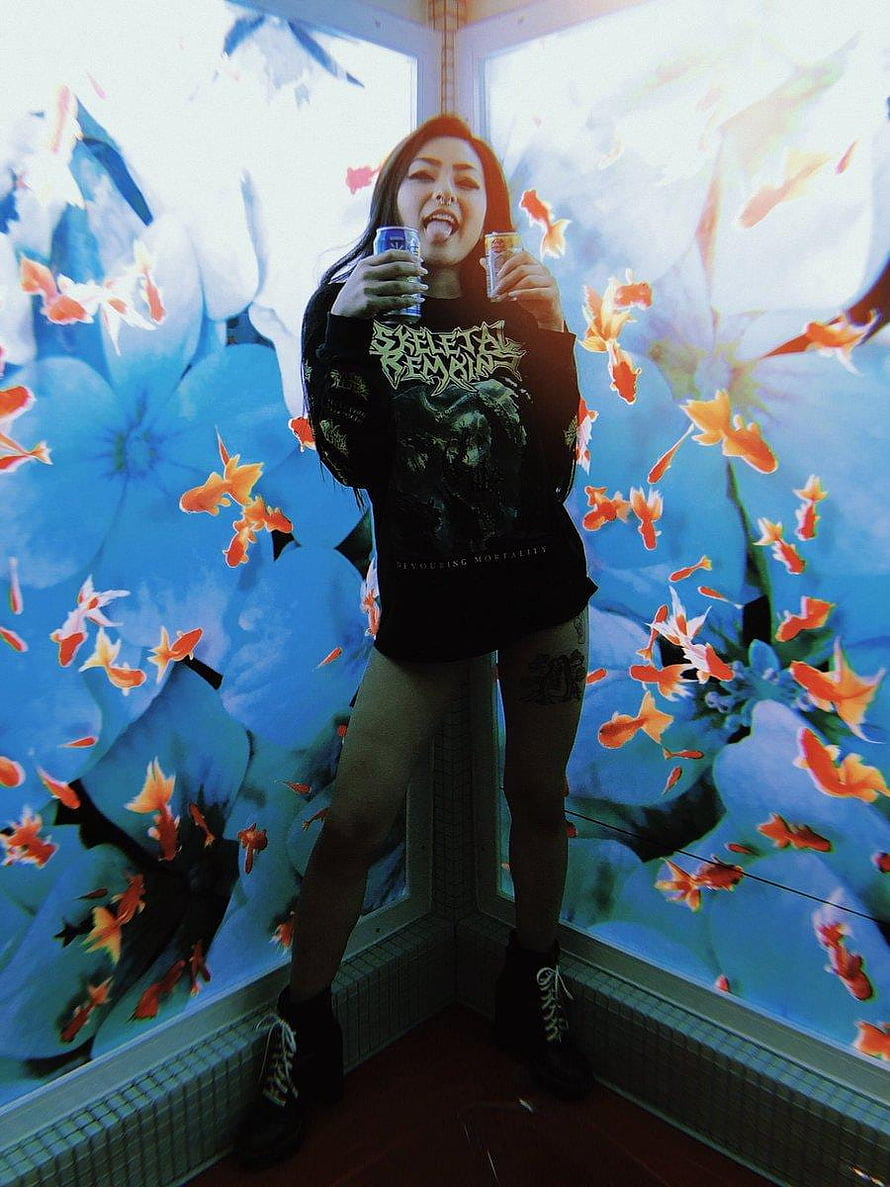 Rae Lil Black in Black Graphic Tee and Combat Boots Against Vibrant Floral and Goldfish Mural HD phone wallpaper