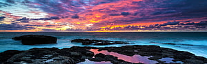 Vibrant Sunset Over Rocky Coastline With Colorful Clouds And Ocean Reflections HD wallpaper