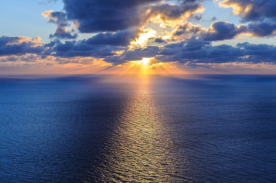 Golden sunset breaking through dramatic clouds over a vast open ocean horizon HD wallpaper