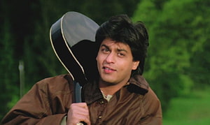 Shah Rukh Khan holding a guitar in a brown jacket from the classic Bollywood film Dilwale Dulhania Le Jayenge HD wallpaper