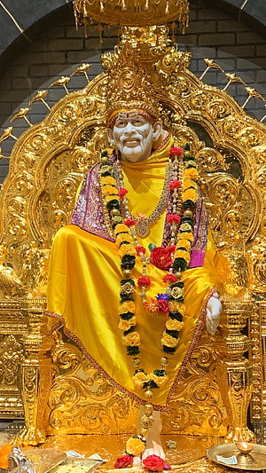 Golden Statue of Sai Baba Seated on Ornate Throne with Flower Garlands HD phone wallpaper