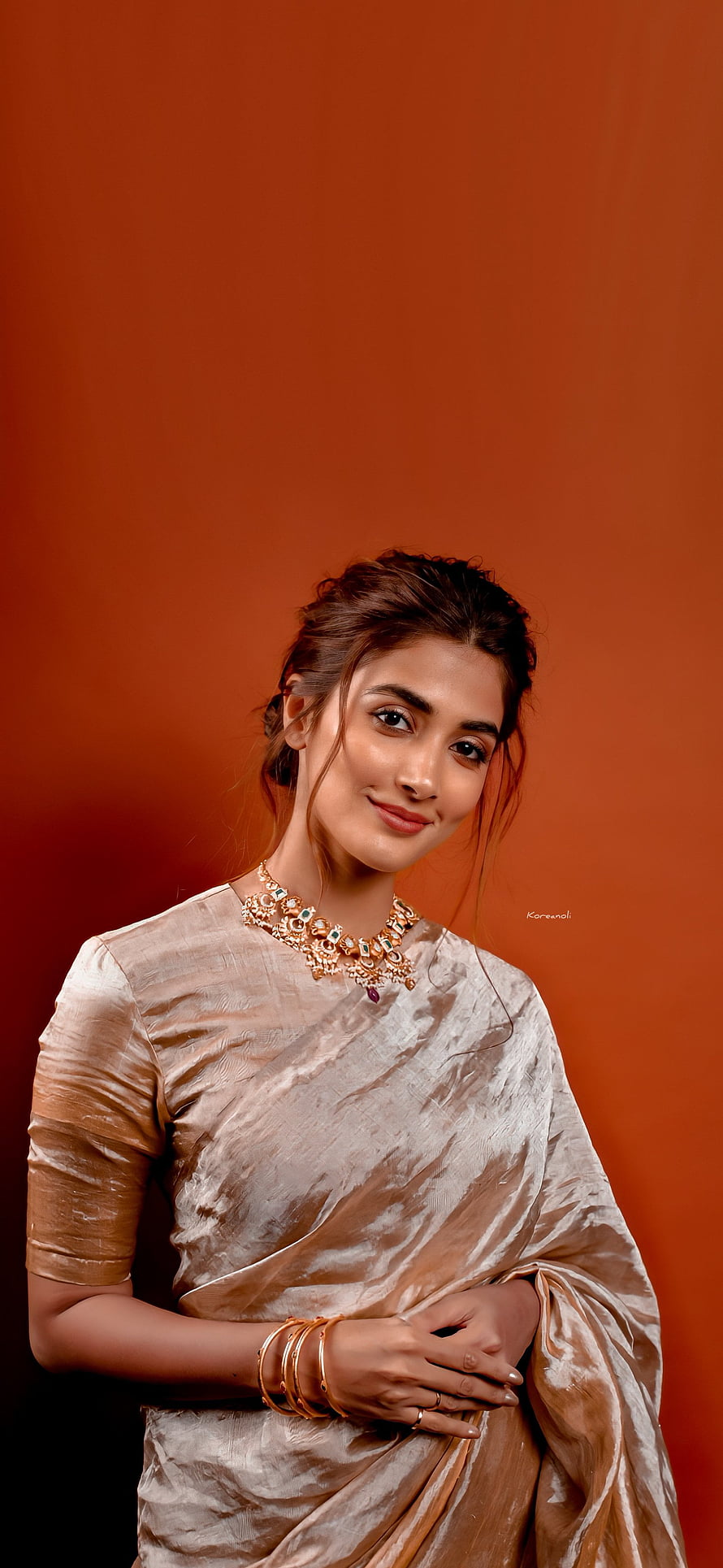 Pooja Hegde in a shimmering beige saree with traditional gold jewelry against a warm orange background HD phone wallpaper