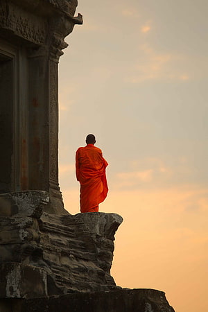 Buddhist monk in saffron robes standing on ancient stone temple ledge at sunset HD phone wallpaper