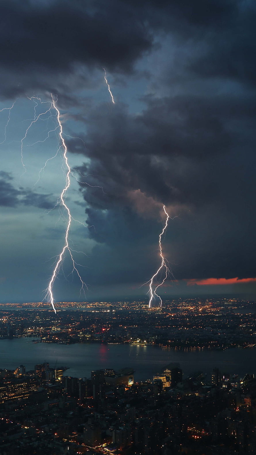 Dramatic lightning strikes over a sprawling city skyline at night with a dark stormy sky HD phone wallpaper