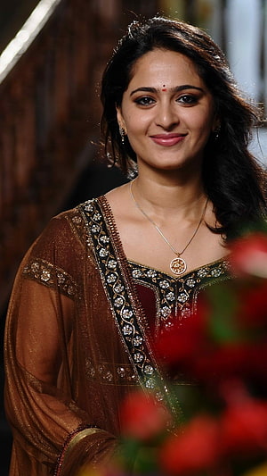 Anushka Shetty in Traditional Indian Ethnic Wear with Gold Jewelry and Floral Background HD phone wallpaper