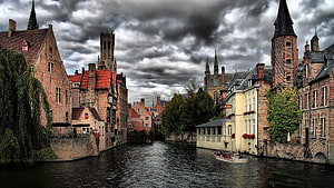 Historic Bruges Canal with Medieval Architecture and Tourist Boat Under Dramatic Sky HD wallpaper