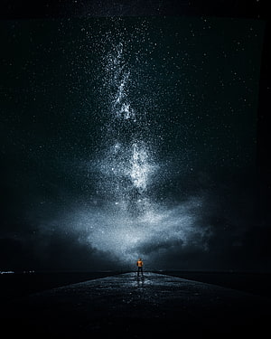 Lone figure standing on a dark pier beneath the vast Milky Way galaxy and starry night sky HD phone wallpaper